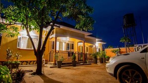 A two-story house with a balcony, a car parked in front, and a water tank in the background. - Urban Oasis (Kampala)