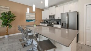 A modern kitchen with a large island, stainless steel appliances, white cabinets, and pendant lighting.