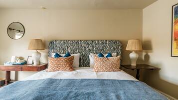A neatly arranged bedroom with a large bed, two bedside tables, a mirror, and a wall-mounted lamp.