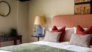 A neatly made bed with a green blanket, a patterned vase with flowers, and a lamp on a bedside table.