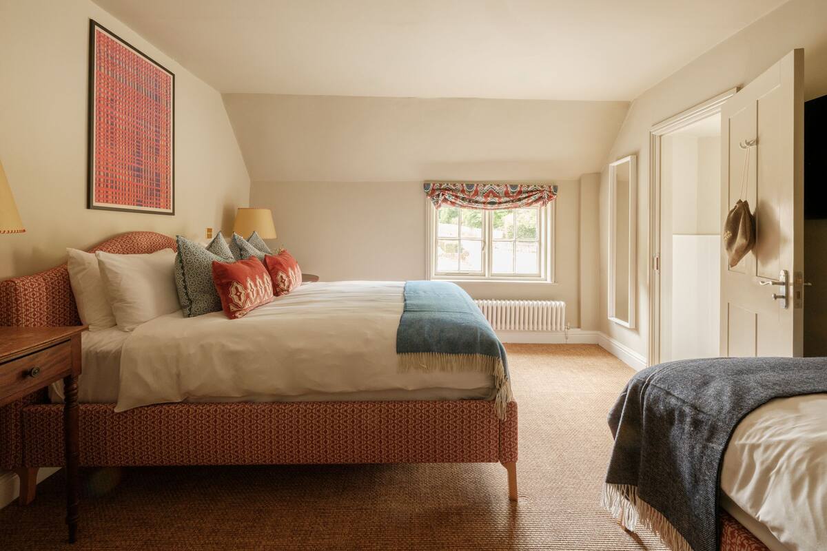 A bedroom with a large bed, a bedside table, a lamp, a window with curtains, and a radiator.