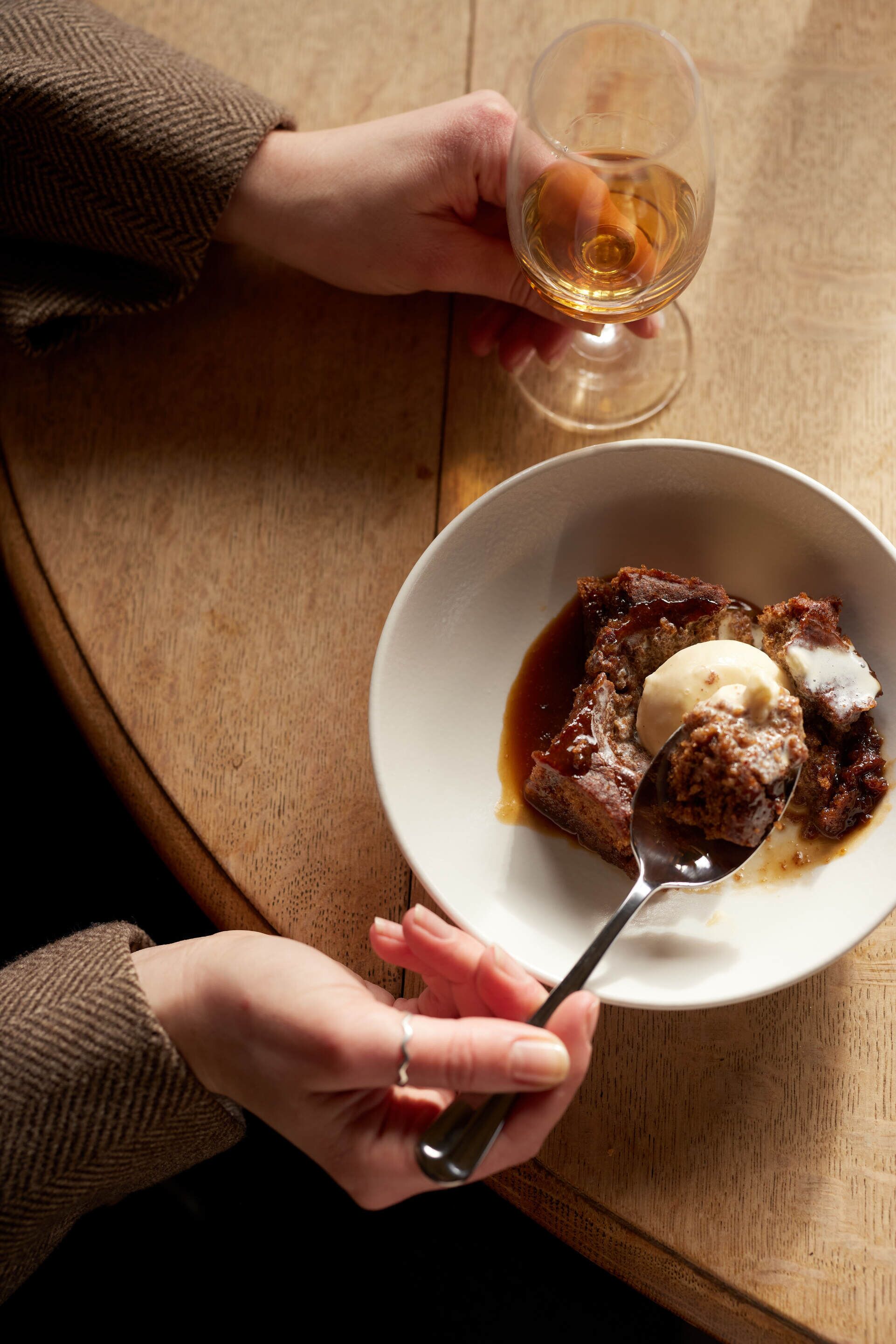 Una persona sosteniendo una copa de vino y un tazón de postre con una cuchara.