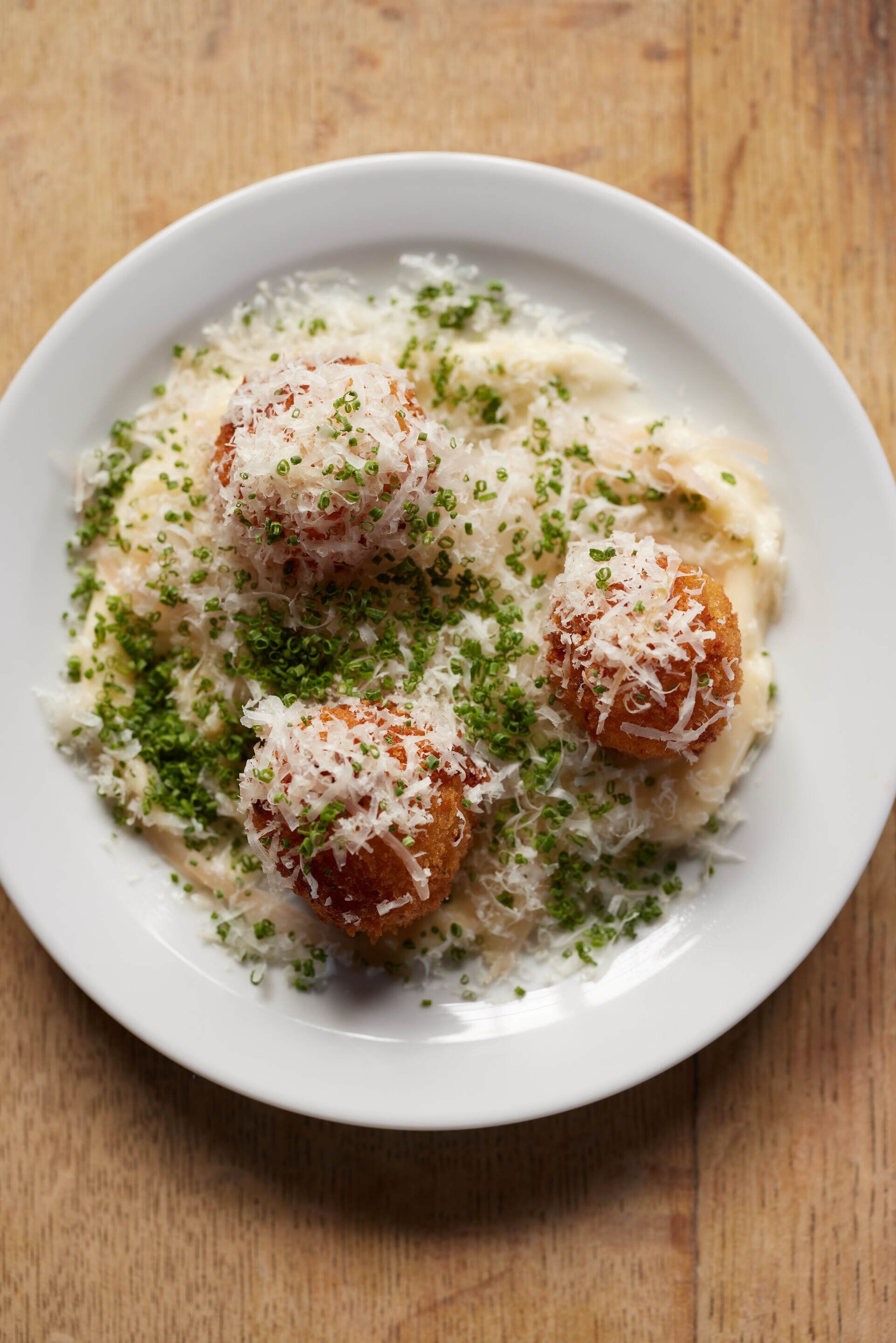 A white plate with a dish of pasta, topped with grated cheese and green herbs.