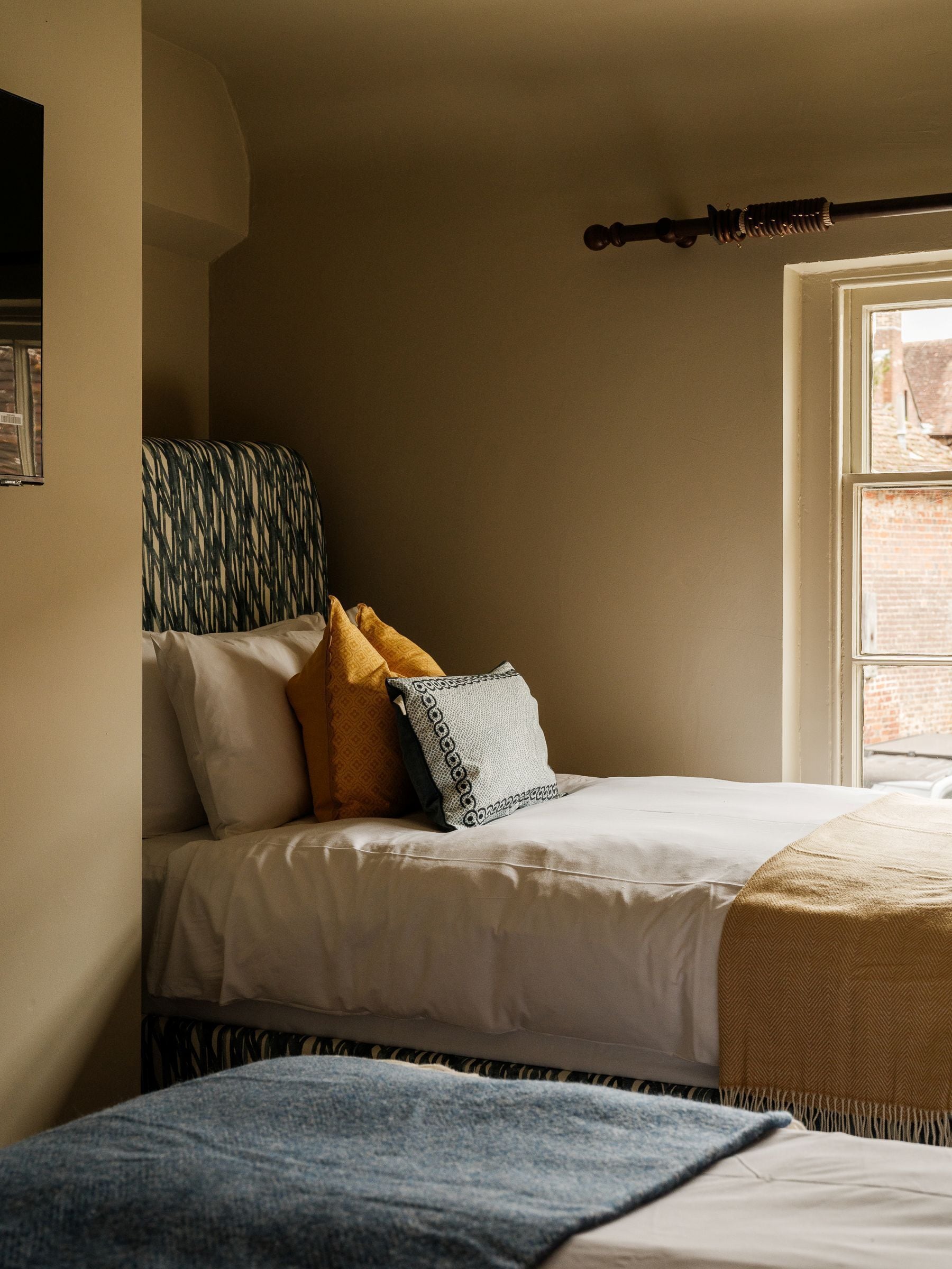 Een slaapkamer met een bed, kussens, een raam en een deur.