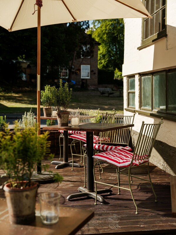 An outdoor patio with a table and chairs, surrounded by potted plants and a large umbrella. - The Fleur de Lys (Cranborne)