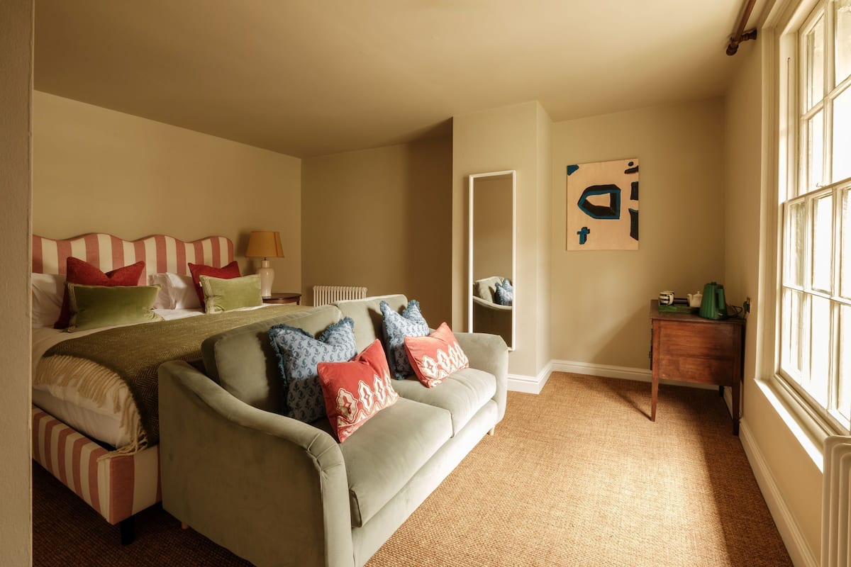 A bedroom with a bed, a sofa, a small table, and a window.