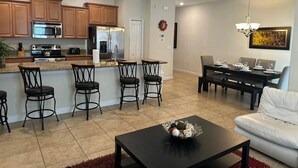Eine moderne Küche mit Edelstahlgeräten, ein Essbereich mit einem schwarzen Tisch und Stühlen sowie ein Wohnzimmer mit einem weißen Sofa und einem Couchtisch.