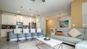 A modern kitchen with white cabinets, a stainless steel refrigerator, and a bar area with white stools. - 4‑Bed Oasis with Pool at Storey Lake (Kissimmee)