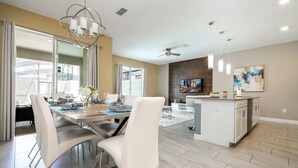 A modern kitchen with a central island, a dining area with white chairs, and a large window providing natural light. - 4‑Bed Oasis with Pool at Storey Lake (Kissimmee)