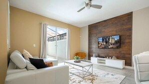 A living room with a sofa, coffee table, and TV on a wooden wall. - 4‑Bed Oasis with Pool at Storey Lake (Kissimmee)