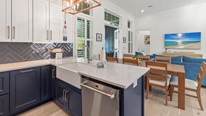 A modern kitchen with white cabinets, a built-in dishwasher, and a wooden dining area with blue upholstered chairs. - Bikes, Private Pool, Putting Green, Close to Seaside and Beach (Santa Rosa Beach)