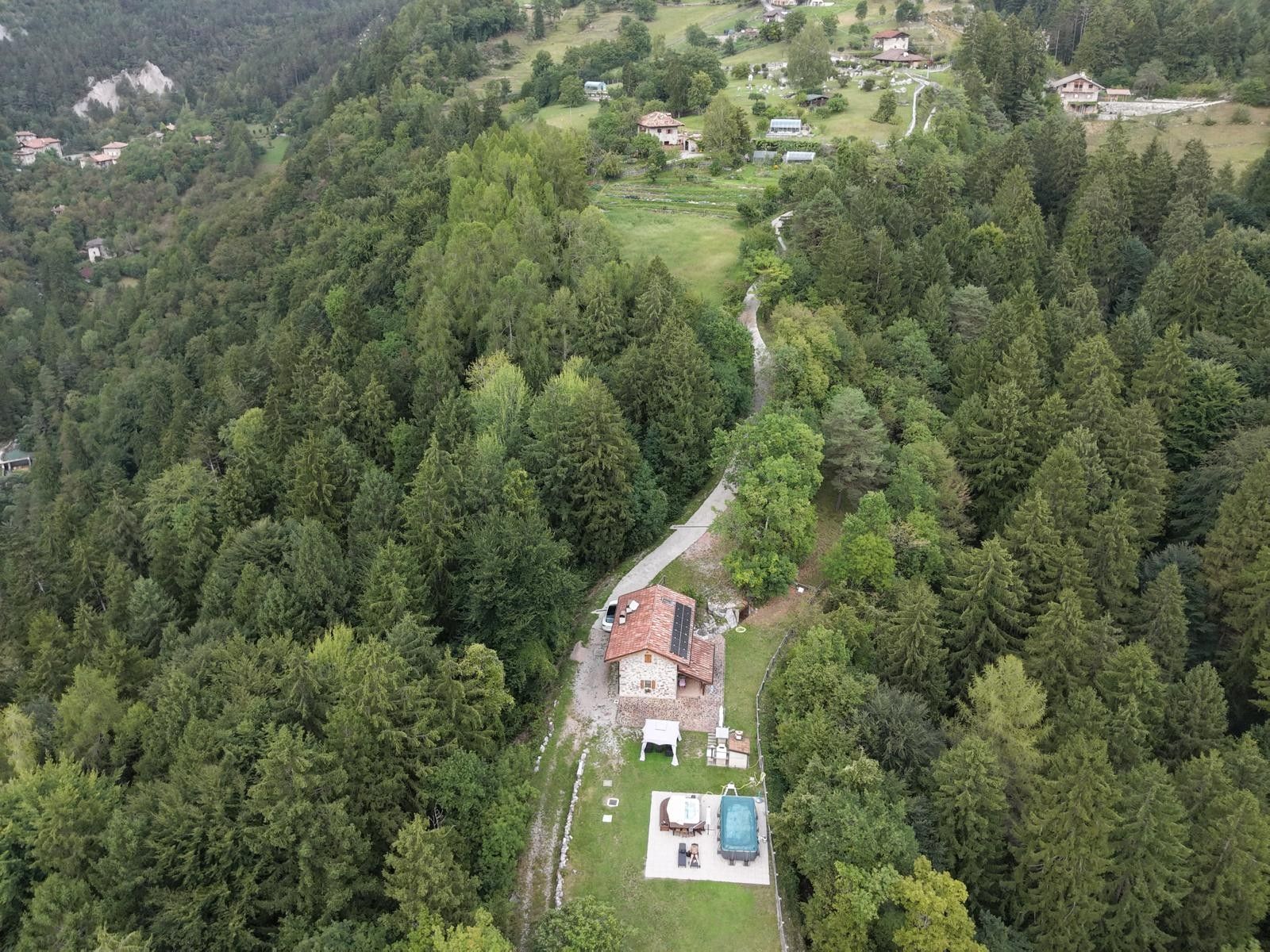 Una casa rodeada de un bosque denso, con una piscina visible y un patio de piedra.
