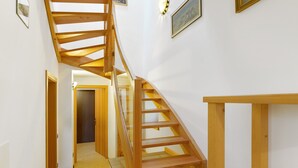 Eine Holztreppe mit Glastrennwand, die zu einem Flur mit weißen Wänden und einer Tür am Ende führt.