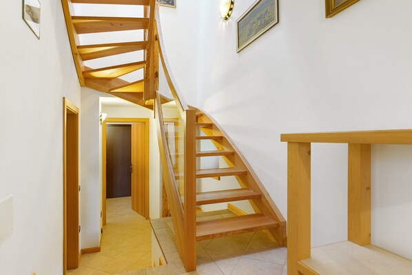 A wooden staircase with a glass railing, leading to a hallway with white walls and a door at the end.