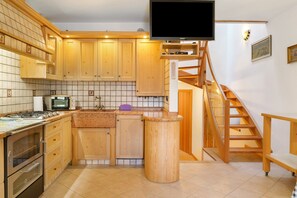 A kitchen with wooden cabinets, a microwave, a stove, and a TV mounted above the counter.