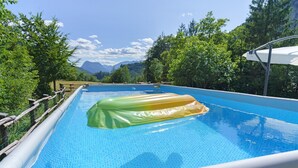 Ein Außenpool mit sechseckigem Fliesenmuster, umgeben von Bäumen und Bergen im Hintergrund.