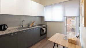 A modern kitchen with grey cabinets, a granite countertop, a built-in oven, and a window with blinds. - Spacious Luxury Apartment | Near Piraeus Port (Piraeus)