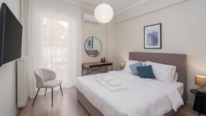 A hotel room with a bed, a chair, a desk, a mirror, and a framed picture on the wall. - Spacious Luxury Apartment | Near Piraeus Port (Piraeus)