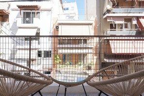 A balcony with wicker chairs and a glass table, overlooking a residential area with buildings and balconies. - Spacious Luxury Apartment | Near Piraeus Port (Piraeus)