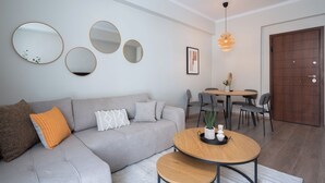 A modern living room with a grey sofa, round mirrors, a dining table with chairs, and a wooden coffee table. - Spacious Luxury Apartment | Near Piraeus Port (Piraeus)
