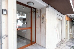 A building entrance with a glass door, a number '24' above the door, and a closed shutter to the right. - Spacious Luxury Apartment | Near Piraeus Port (Piraeus)