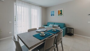 A dining area with a table set for two, a teal sofa, and a small side table. - Modern apartment with pool a few steps from Lake Garda (Padenghe Sul Garda)