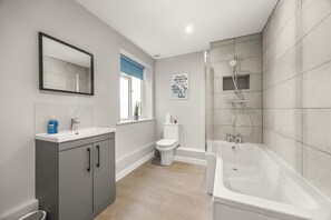 A modern bathroom with a bathtub, toilet, sink, and mirror. - Buzzing Brighton Apartments | By My Getaways (Brighton)
