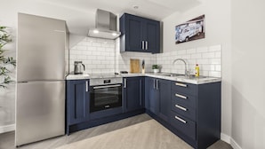 A modern kitchen with dark blue cabinets, white subway tiles, stainless steel appliances, and a small island with a sink. - Buzzing Brighton Apartments | By My Getaways (Brighton)