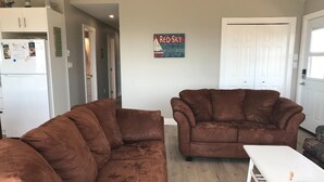 Ein Wohnzimmer mit zwei braunen Sofas, einem weißen Couchtisch und einer Küchenzeile mit Kühlschrank und Schränken.