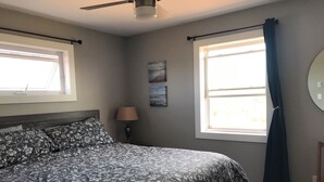 Ein Schlafzimmer mit einem Bett, zwei Fenstern, einer Lampe und einem Sessel.