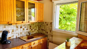 Una cocina con armarios de madera, salpicadero de azulejos, ventana con vistas a vegetación y una cafetera sobre la encimera.