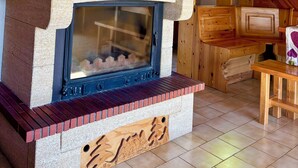 Un interior rústico de madera con chimenea de piedra, un reloj de madera y una ventana con vista a follaje verde.