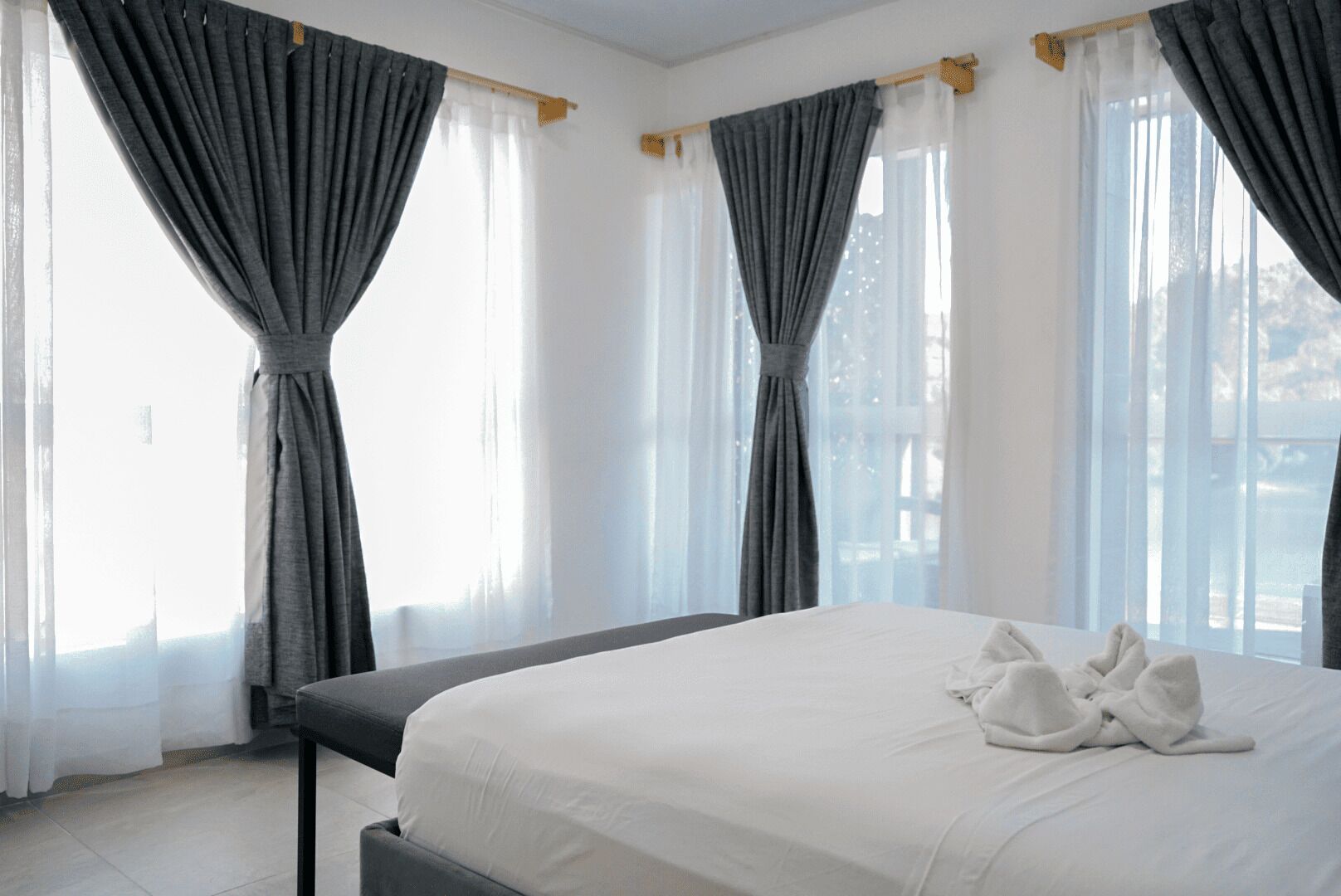 Un cuarto de hotel con una cama grande, cortinas grises y vista al exterior.