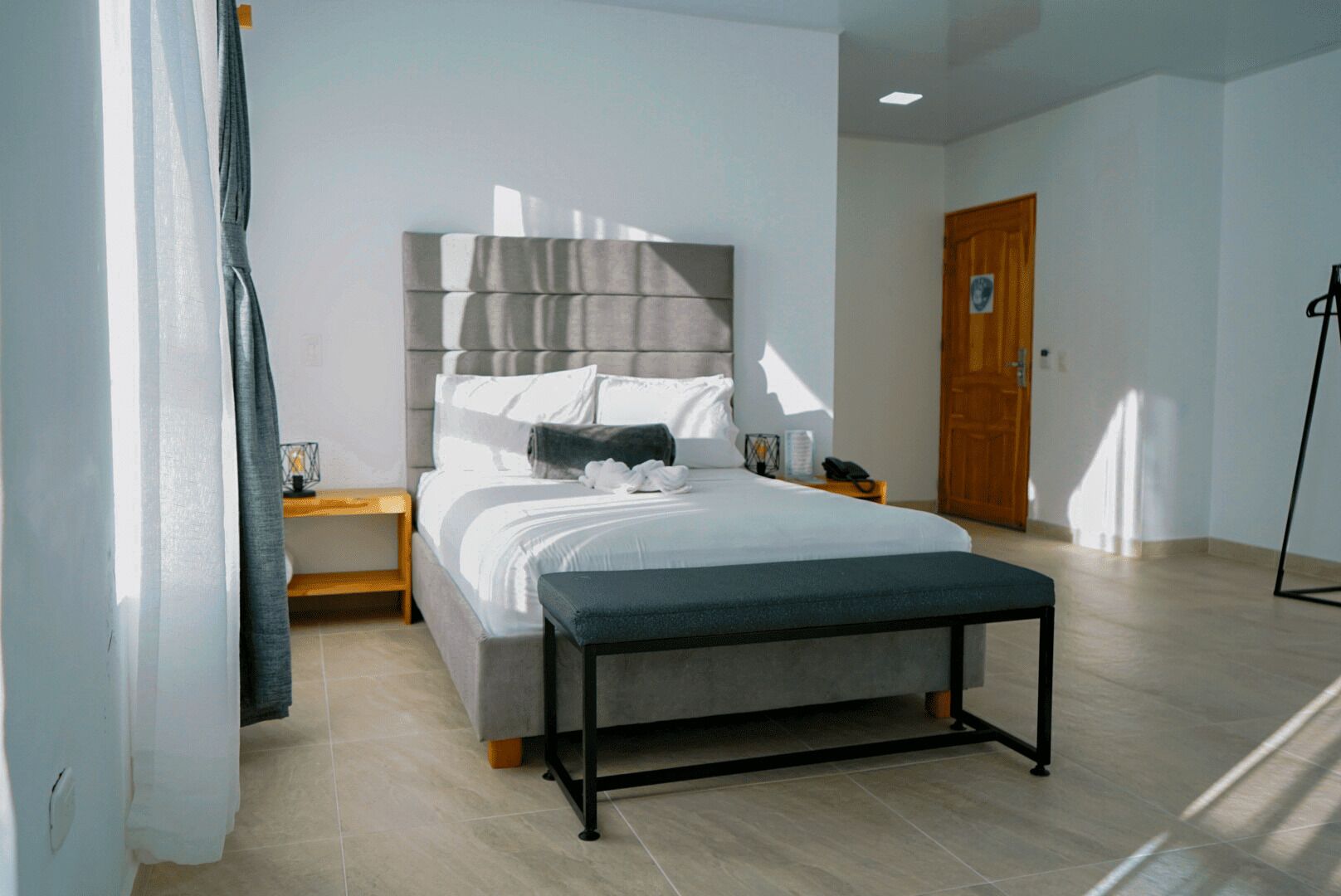 Un dormitorio moderno con una cama grande, mesitas de noche, un banco y una puerta de madera.