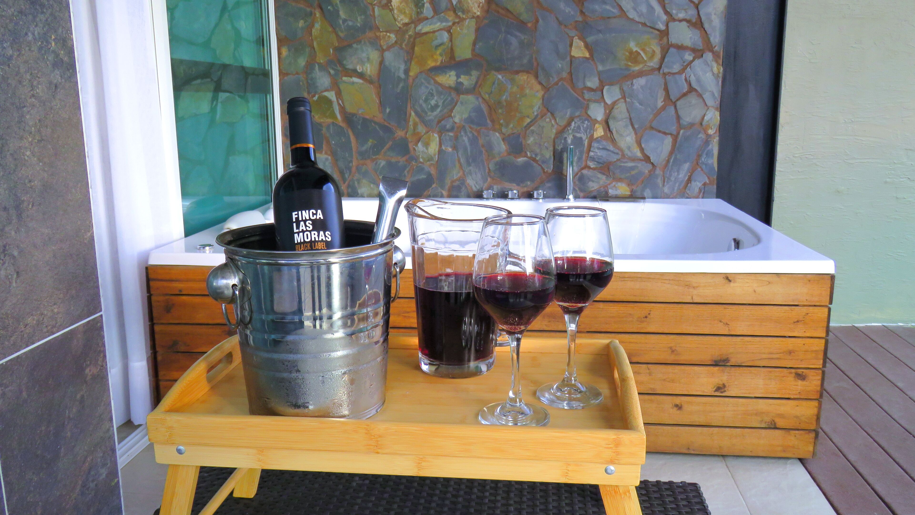Una bandeja de madera con una botella de vino y copas en una terraza.