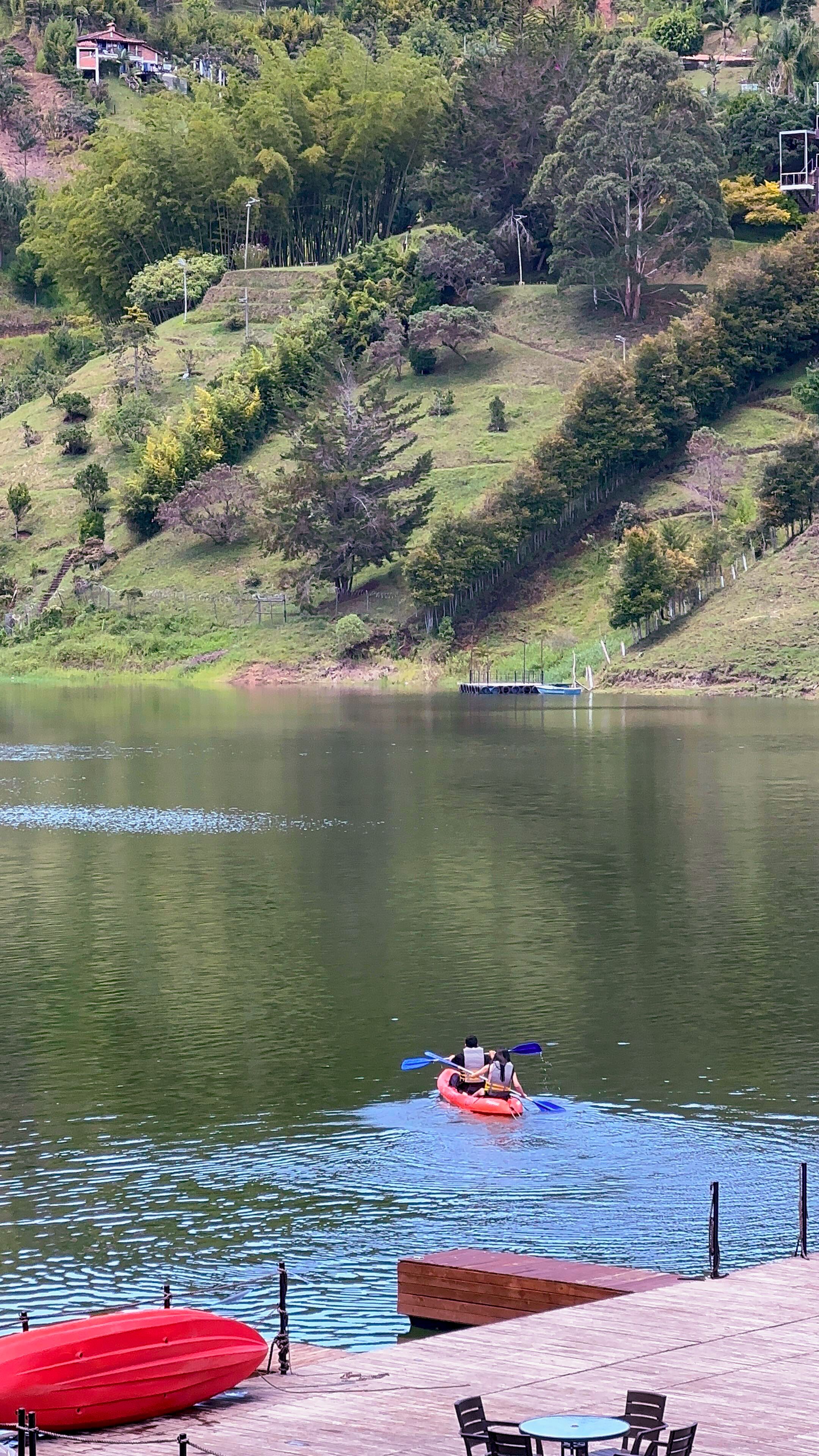 A calm lake with a red kayak and a red boat docked on the shore.