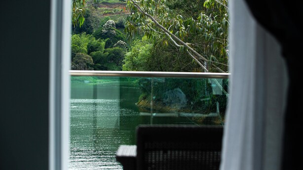 A view from a window overlooking a lush green landscape with a body of water and a chair in the foreground. - Hotel Nova El Peñol (El Peñol)