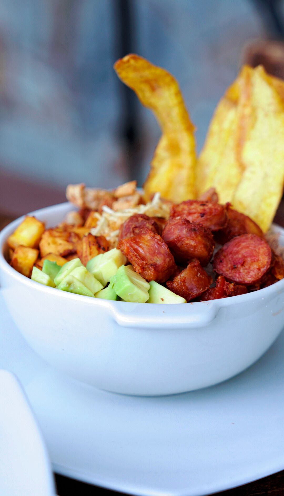Un plato de comida con papas, aguacate y salchicha.