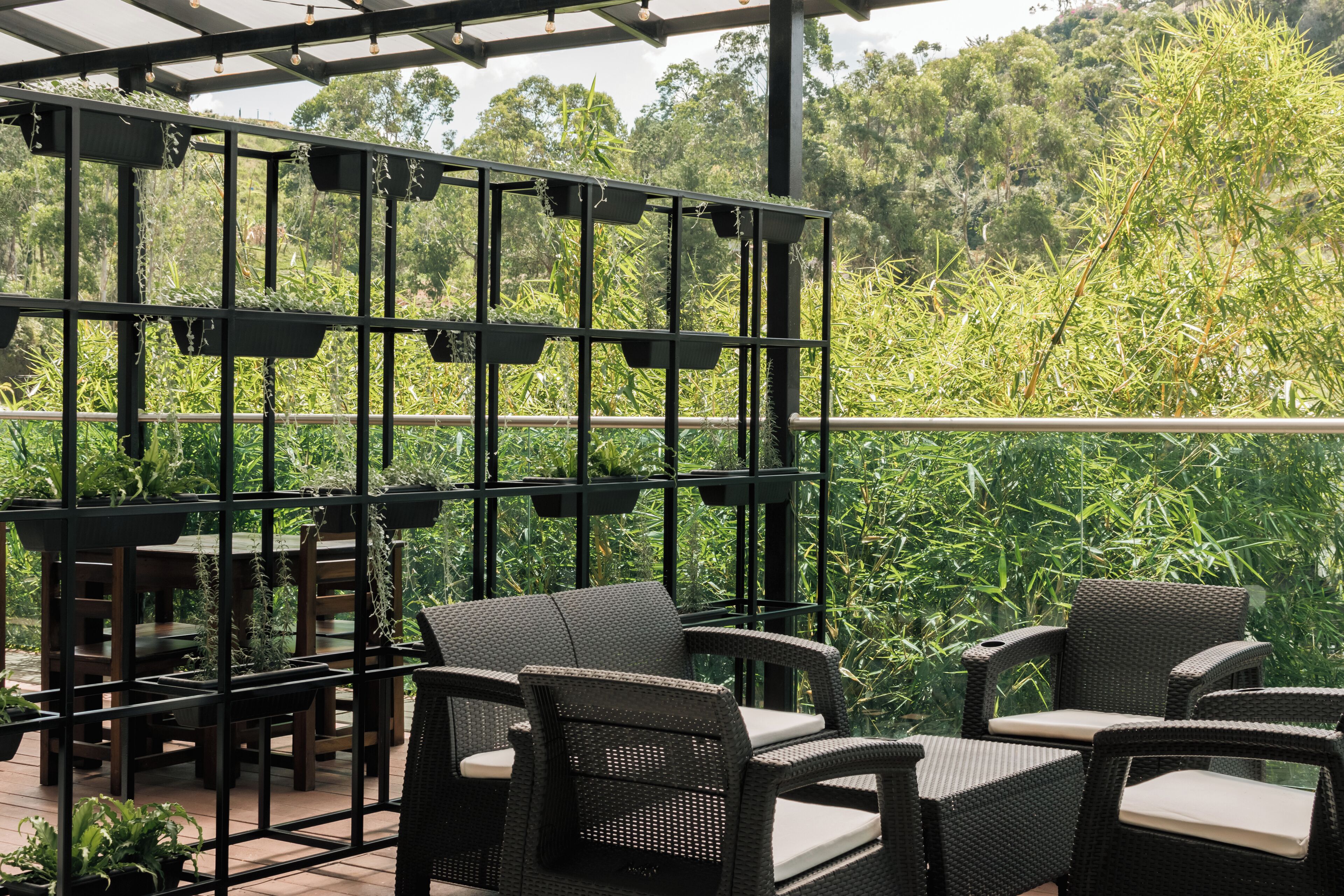 Een terras buiten met rieten meubilair en een zwart metalen trellis met hangplanten.