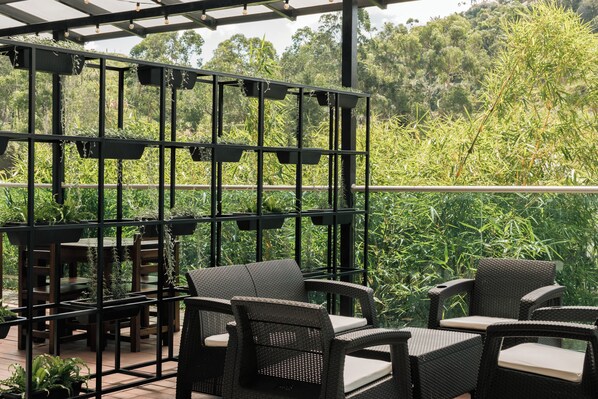 An outdoor patio with wicker furniture and a black metal trellis with hanging planters.