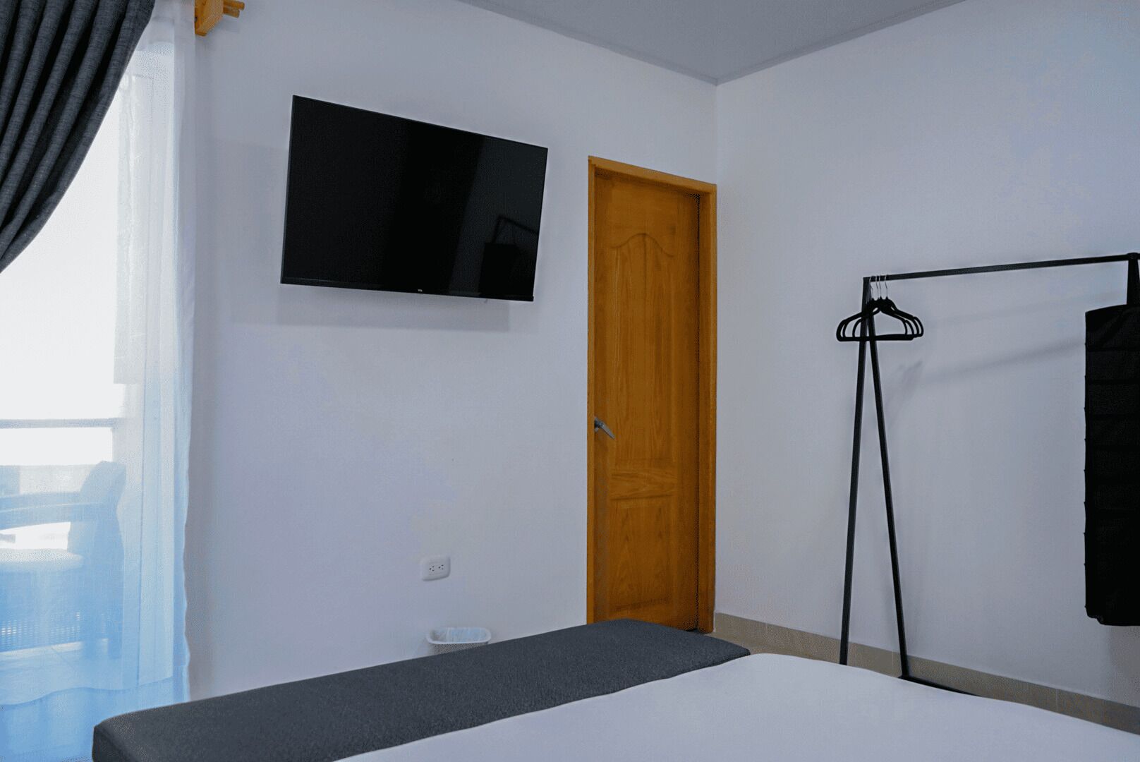 Une chambre d’hôtel avec un lit, un téléviseur fixé au mur, une porte en bois et un porte-manteau.