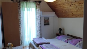 A bedroom with a wooden ceiling, a bed with purple bedding, a bedside table with a vase of flowers, and a window with floral curtains.