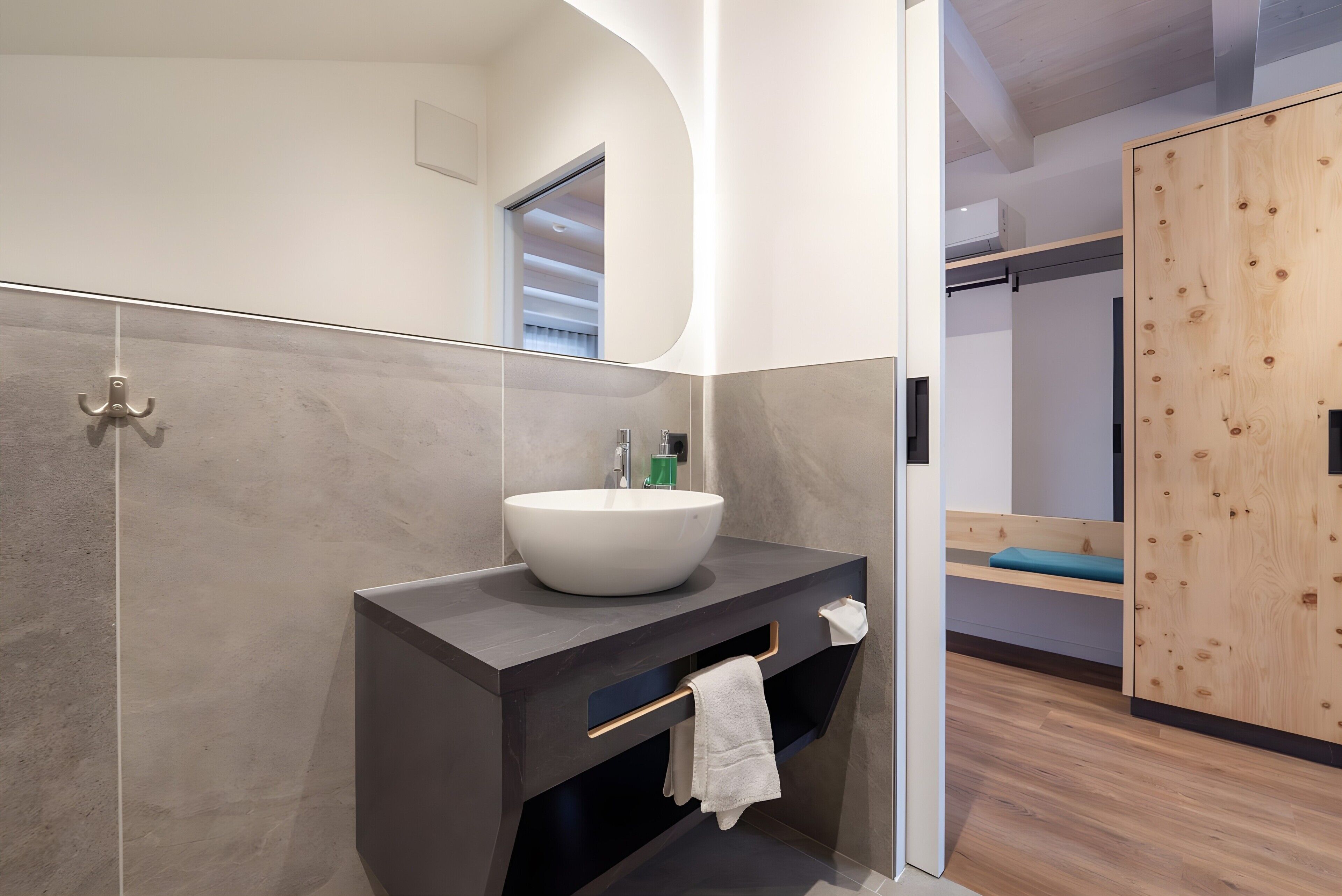 A modern bathroom with a large vessel sink, dark vanity, and a wooden wardrobe.