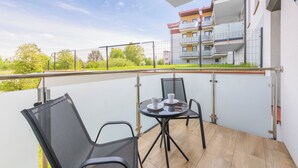 A balcony with a table and chairs, a view of a building, and a fenced area. - Apartamenty Sun & Snow Perła Mierzei (Sztutowo)