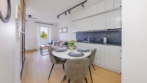 A modern kitchen with white cabinets, a black countertop, and a dining area with a round table set for four. - Apartamenty Sun & Snow Perła Mierzei (Sztutowo)