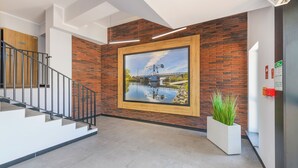 A modern interior with a staircase, a large framed picture of a bridge over water, and a potted plant. - Apartamenty Sun & Snow Perła Mierzei (Sztutowo)