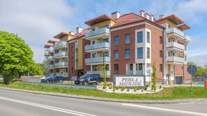 A multi-story residential building with balconies, a sign indicating 'PERLA MERZEI,' and a parking area with cars. - Apartamenty Sun & Snow Perła Mierzei (Sztutowo)
