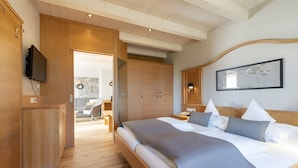 A modern bedroom with a large bed, wooden wardrobe, and a television mounted on the wall.