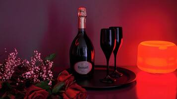 A bottle of Ruinart champagne, two wine glasses, a lit candle, and a bouquet of flowers on a table.