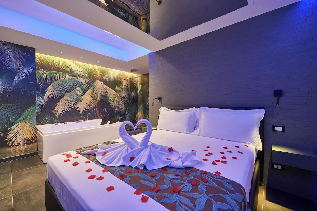 A modern hotel room with a large bed, a bathtub, and a mural of palm trees.